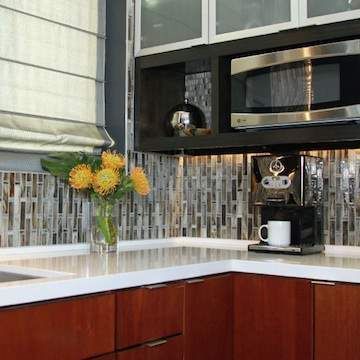 A kitchen with a microwave , coffee maker , and a vase of flowers on the counter.
