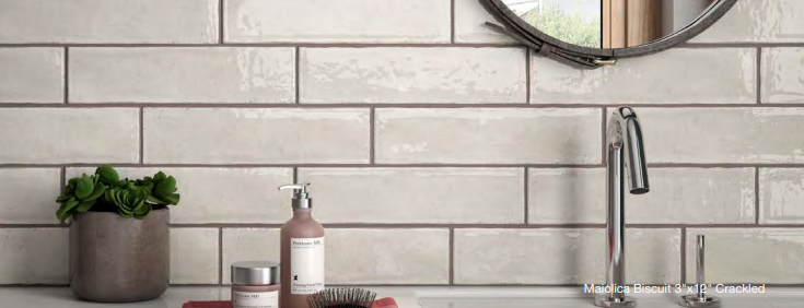 A bathroom with white tiles , a sink , a mirror and a plant.