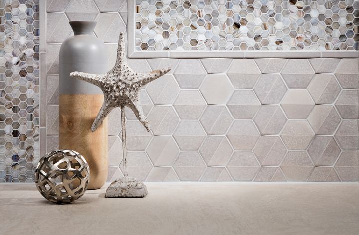 A vase , starfish , and ball are on a table in front of a tiled wall.