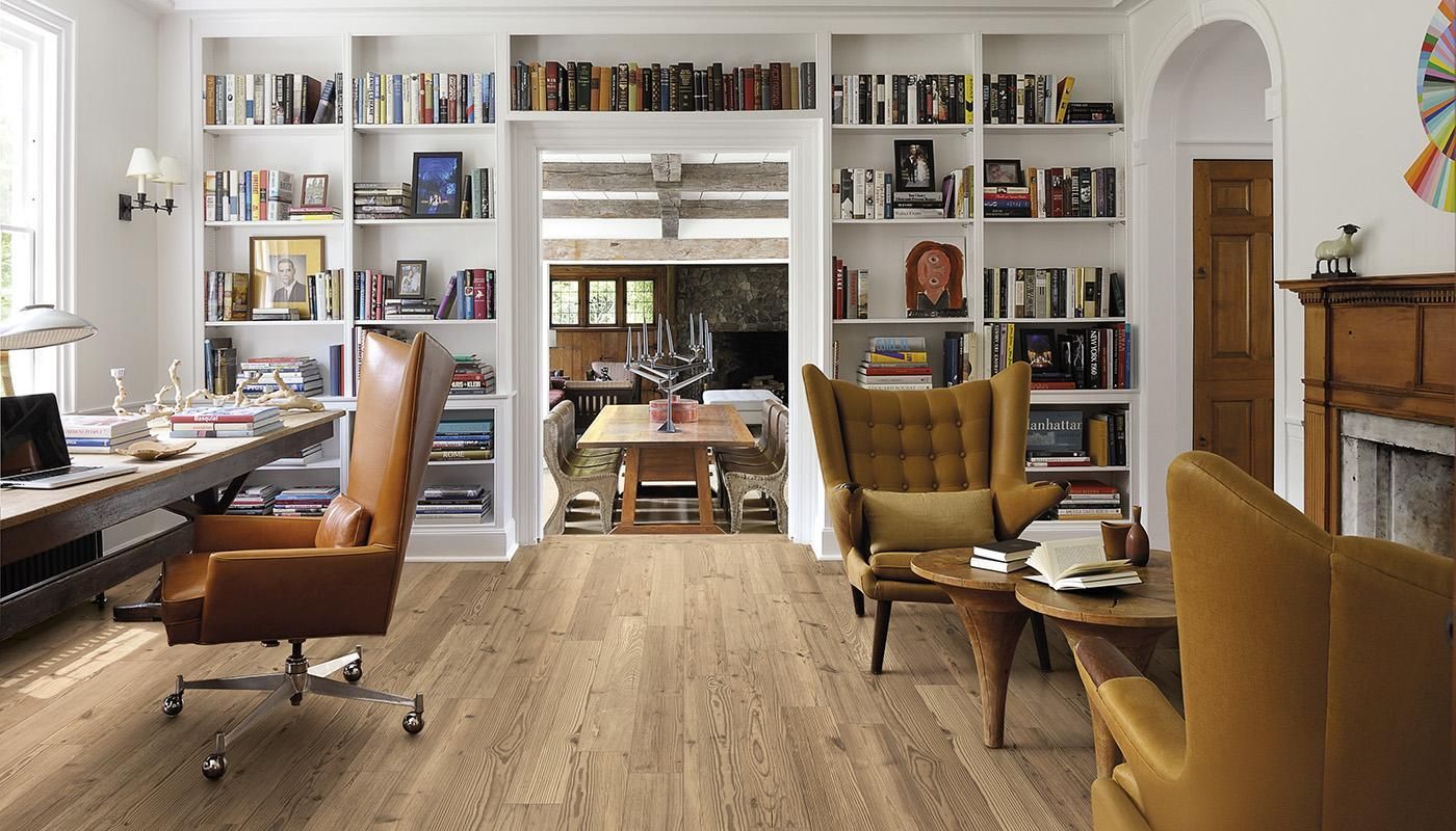 A living room with hardwood floors , a desk , chairs , bookshelves and a fireplace.