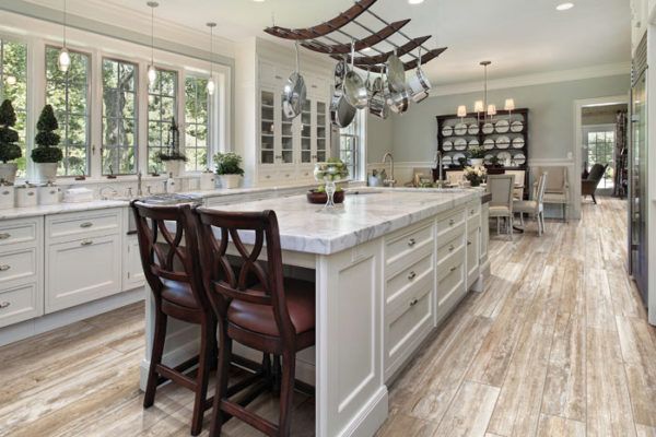 A kitchen with white cabinets , a large island , and wooden floors.