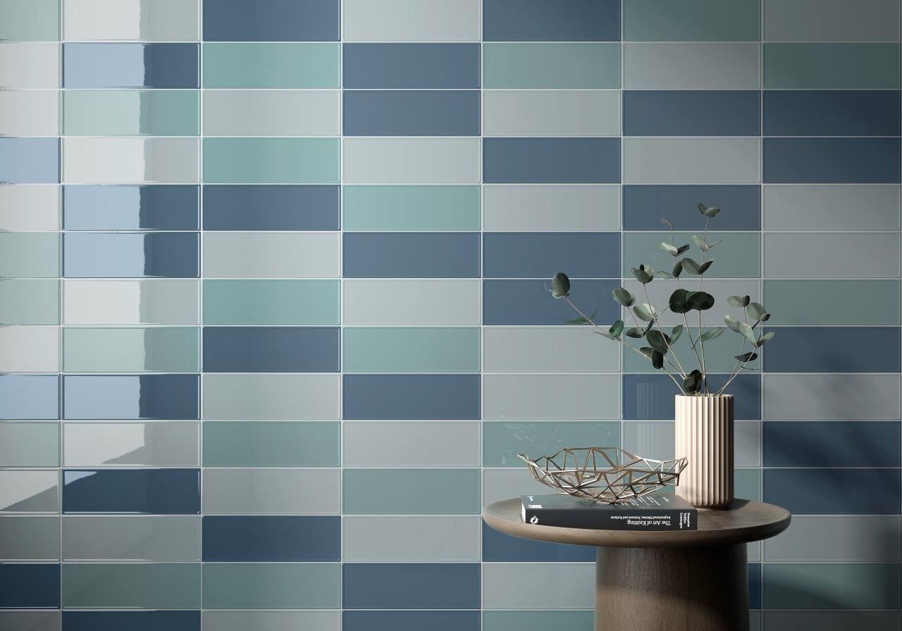 A table with a vase of flowers on it in front of a wall with blue tiles.