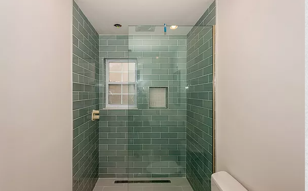 A bathroom with green tiles and a walk in shower with a glass door.