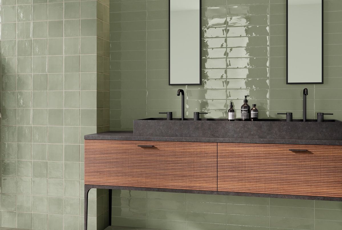 A bathroom with two sinks , two mirrors and green tiles.