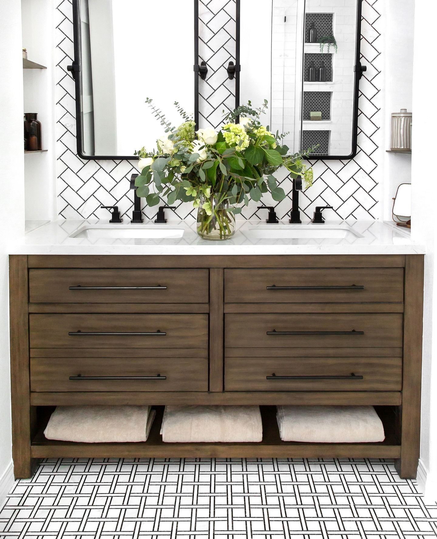 A bathroom with two sinks , a mirror and a vase of flowers.