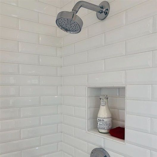 A shower with a shower head and a bottle of soap on a shelf.