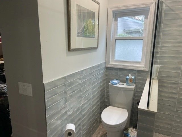A bathroom with a toilet , shower and window.