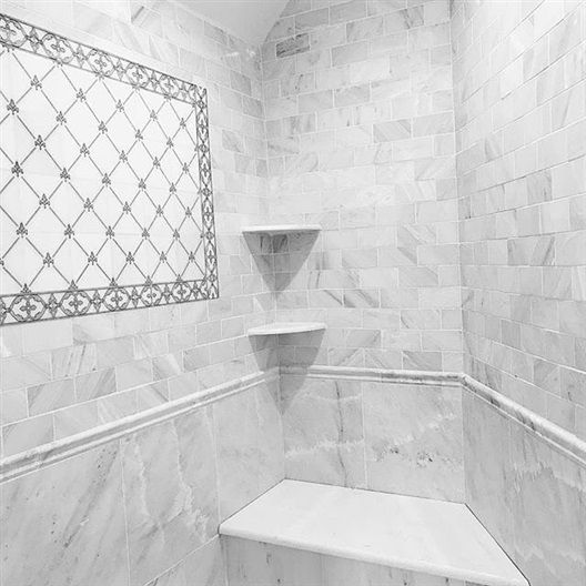 A white tiled shower with a bench and shelves.