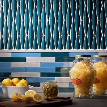 A kitchen with blue and white tiles , lemons , jars of pineapple , and a cutting board.