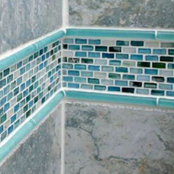 A corner of a shower with blue and white tiles.