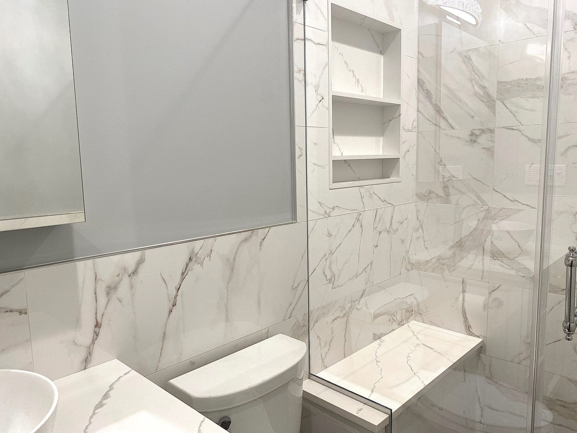 A bathroom with a toilet , sink , mirror and walk in shower.