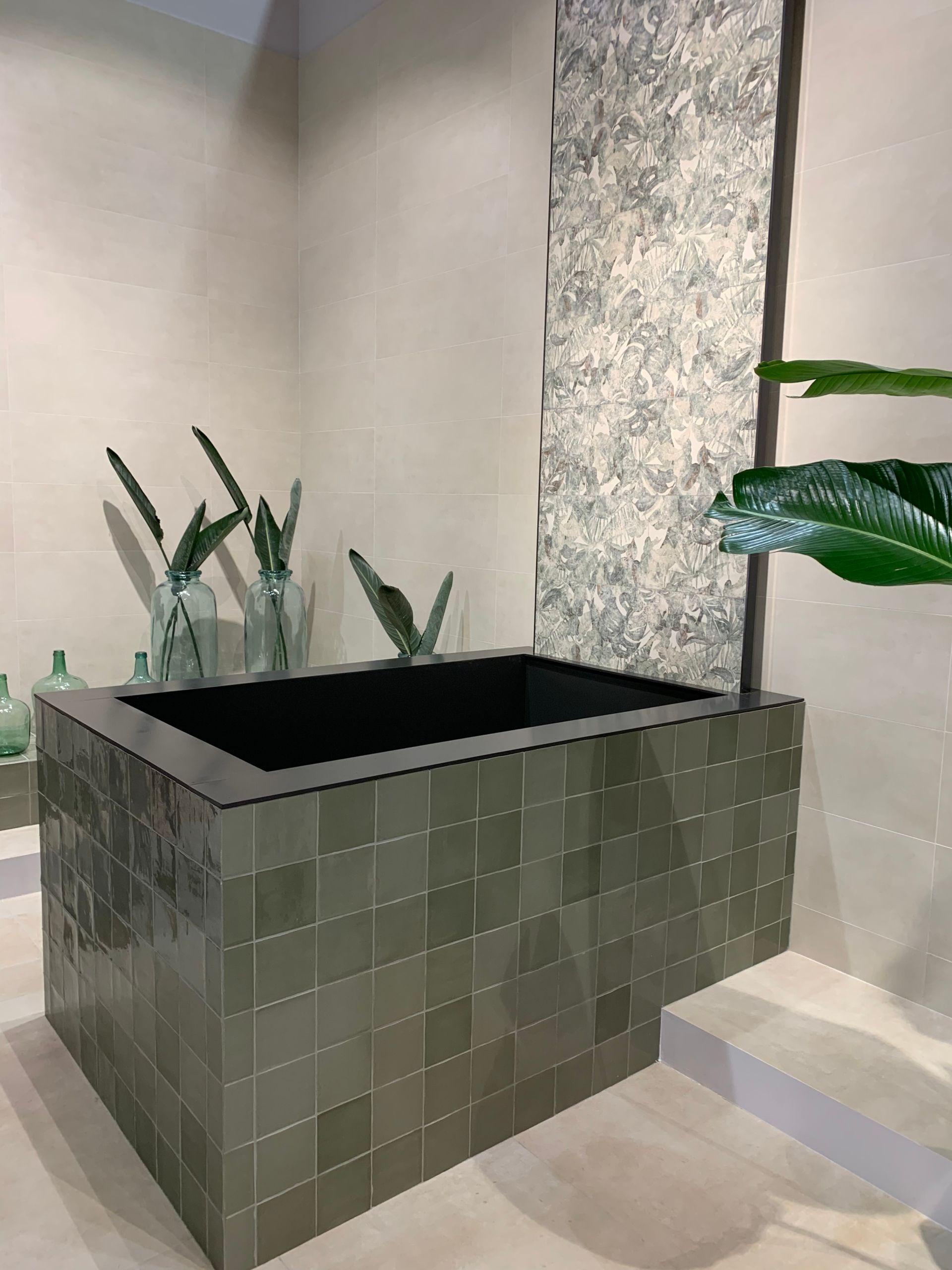 A bathtub surrounded by green tiles in a bathroom.