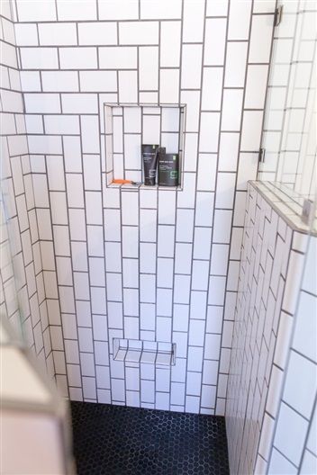A shower with white tiles and a black floor