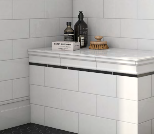 A bathroom with white tiles and a shelf with bottles on it