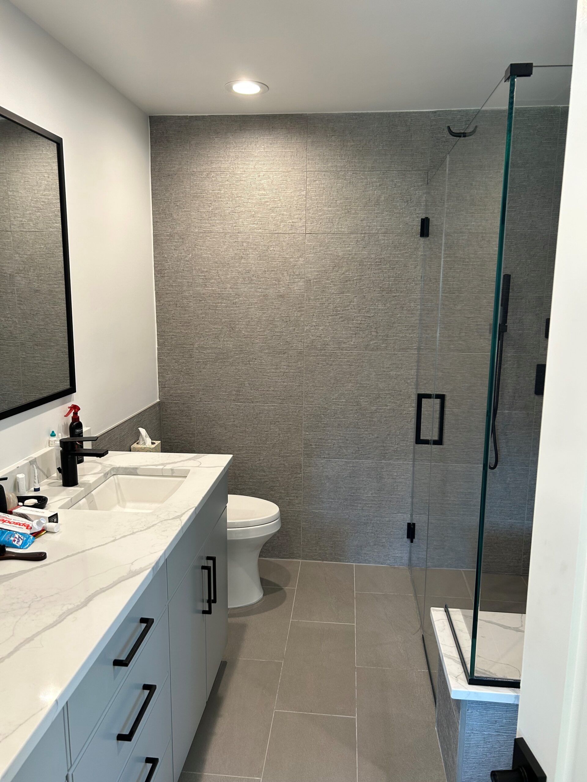 A bathroom with a toilet , sink , mirror and walk in shower.