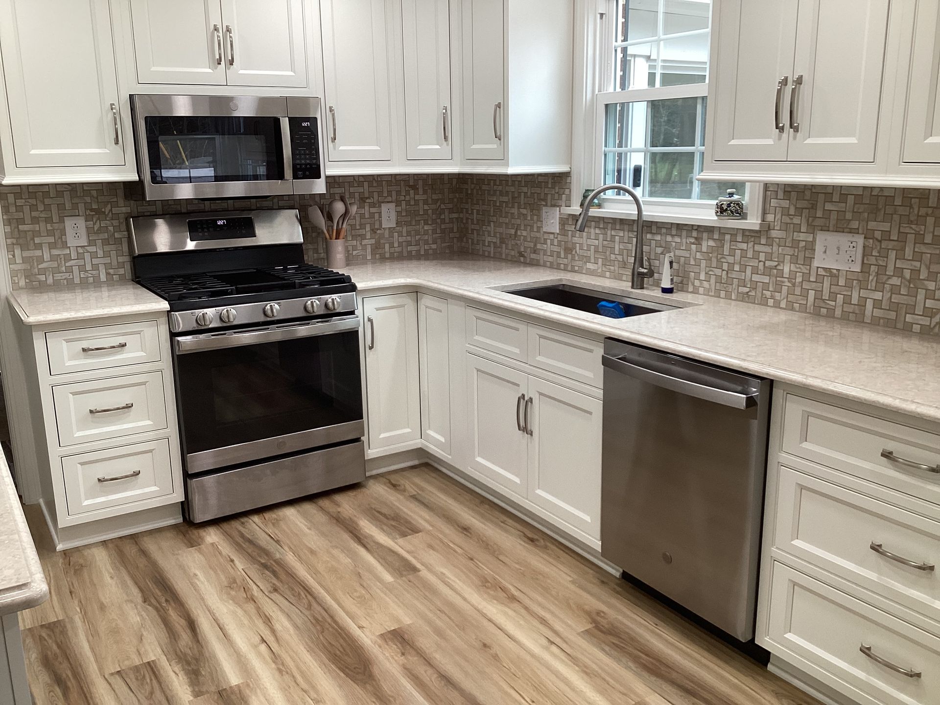 White kitchen with stainless steel appliances, light countertops, wood-look floor, and tiled backsplash.