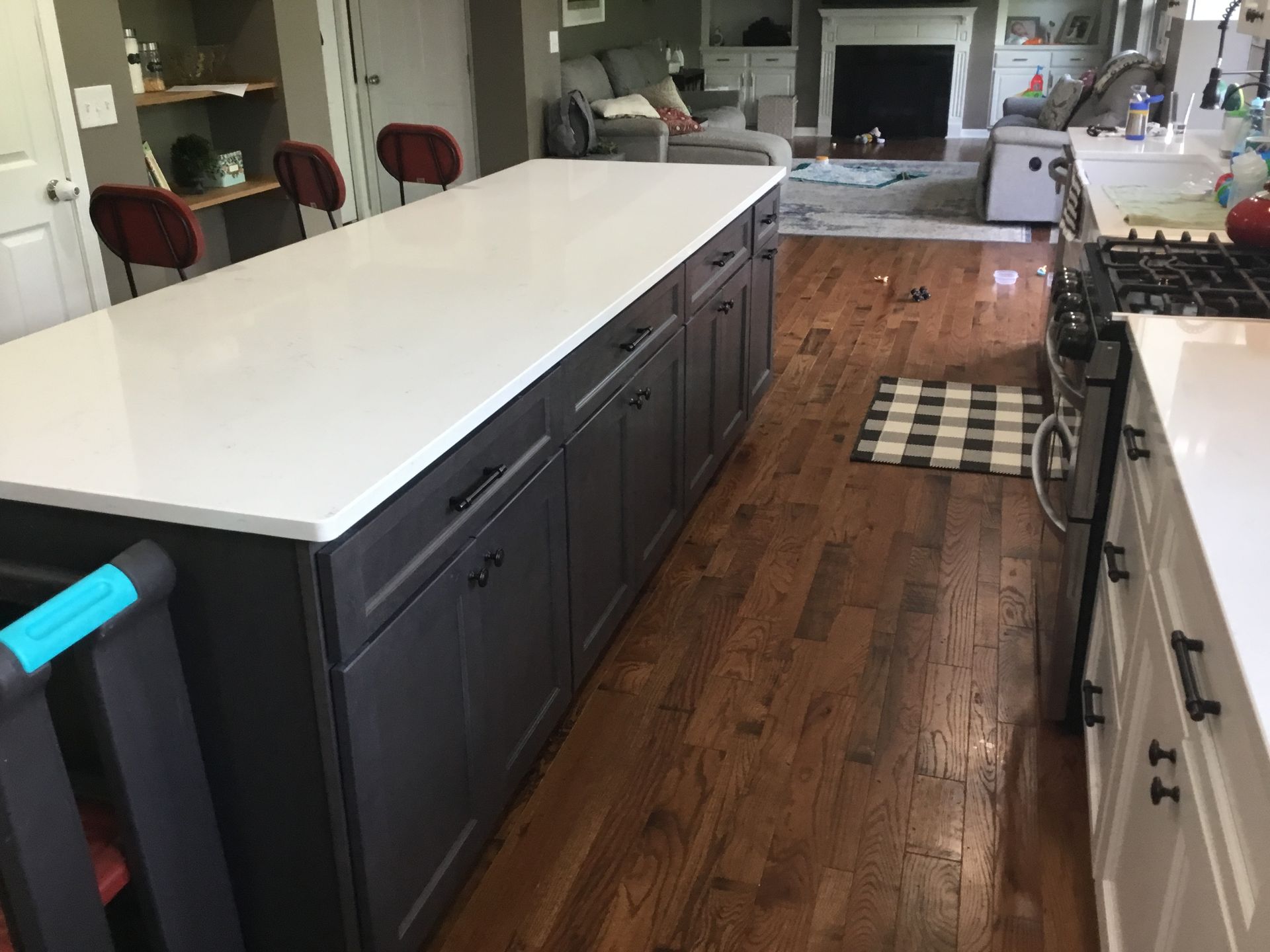 Kitchen with a large island, dark gray cabinets, white countertop, and hardwood floors.