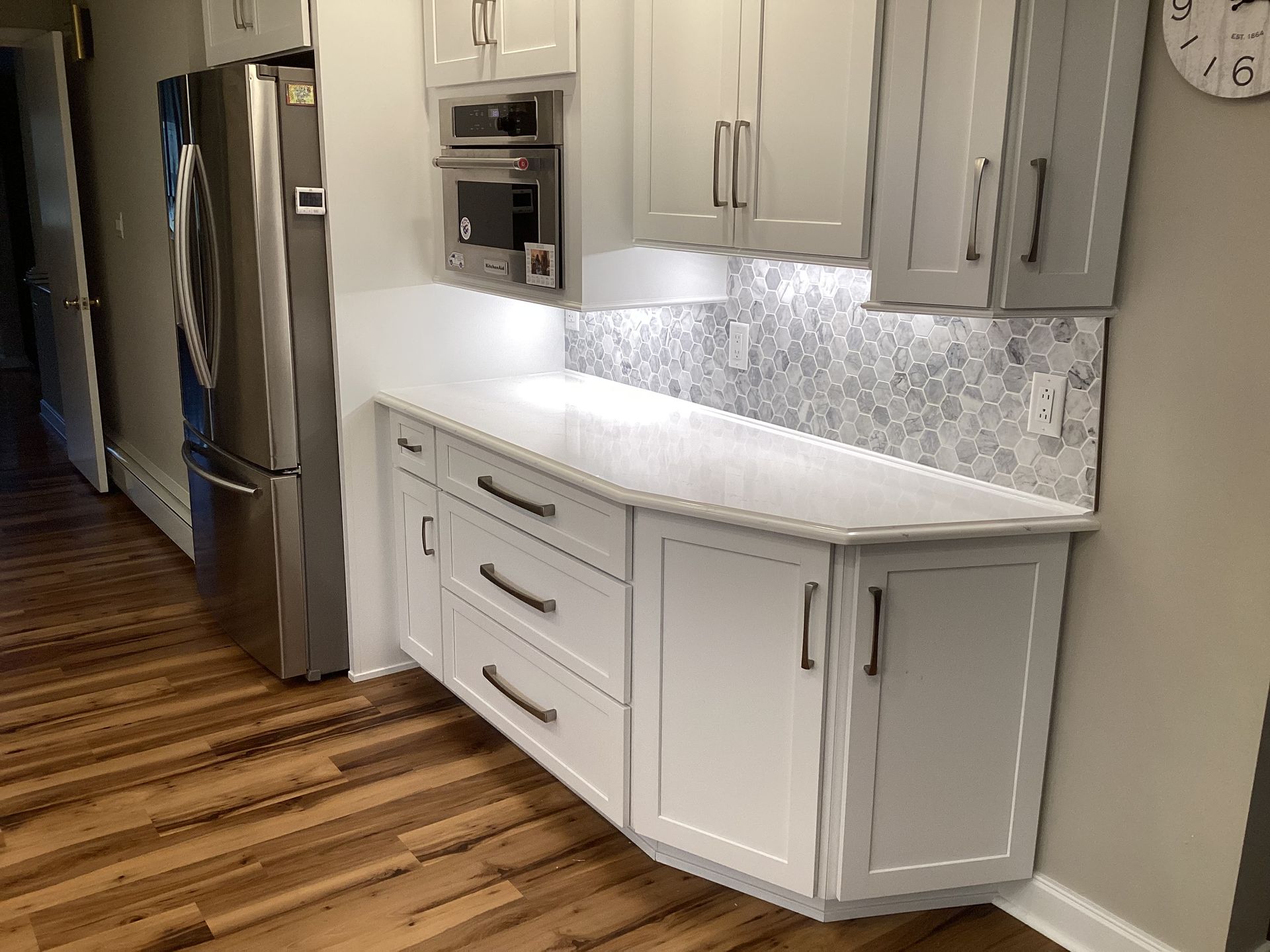 Kitchen cabinetry with white countertops, backsplash, and appliances against a wall.