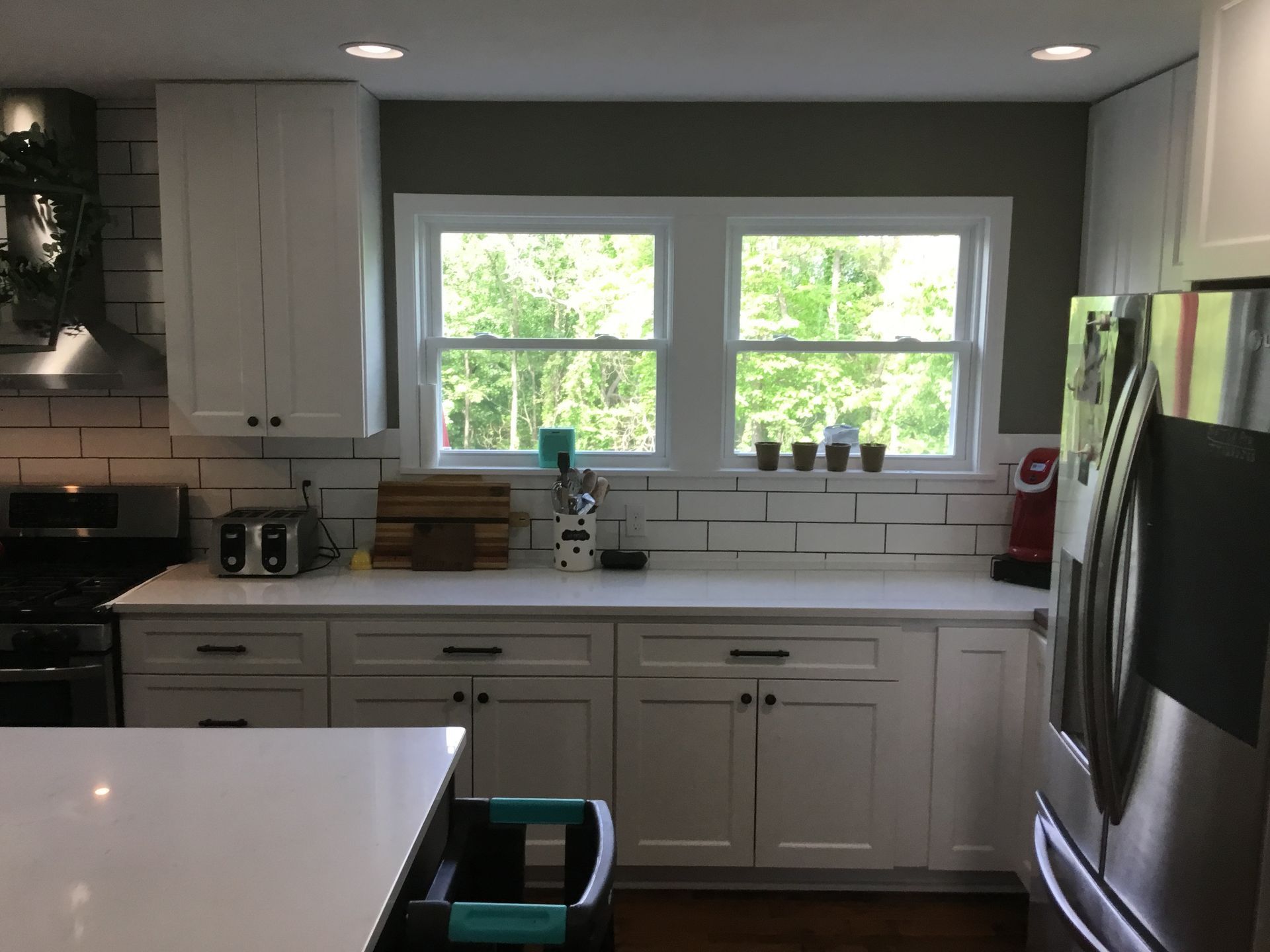 White kitchen with cabinets, countertops, and appliances; windows overlook greenery.