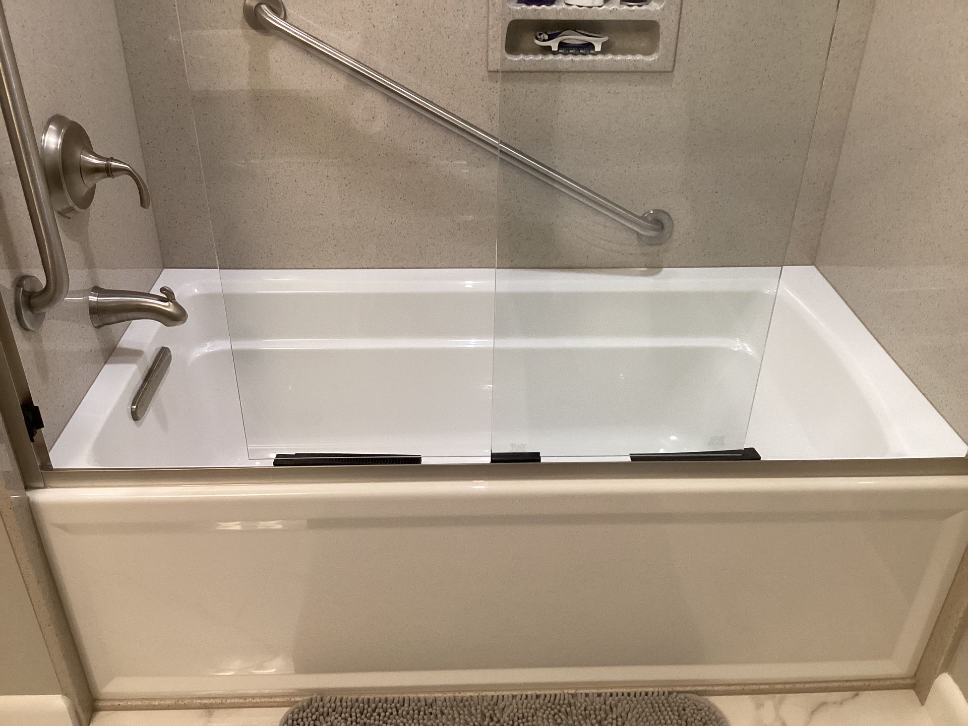 White bathtub with glass shower doors and grab bar in a bathroom.