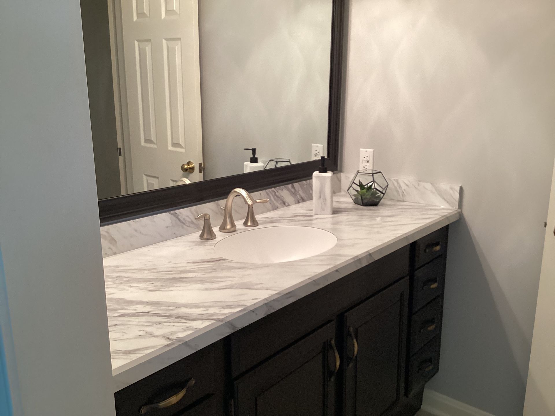 Bathroom vanity with marble countertop, dark cabinets, and large mirror.