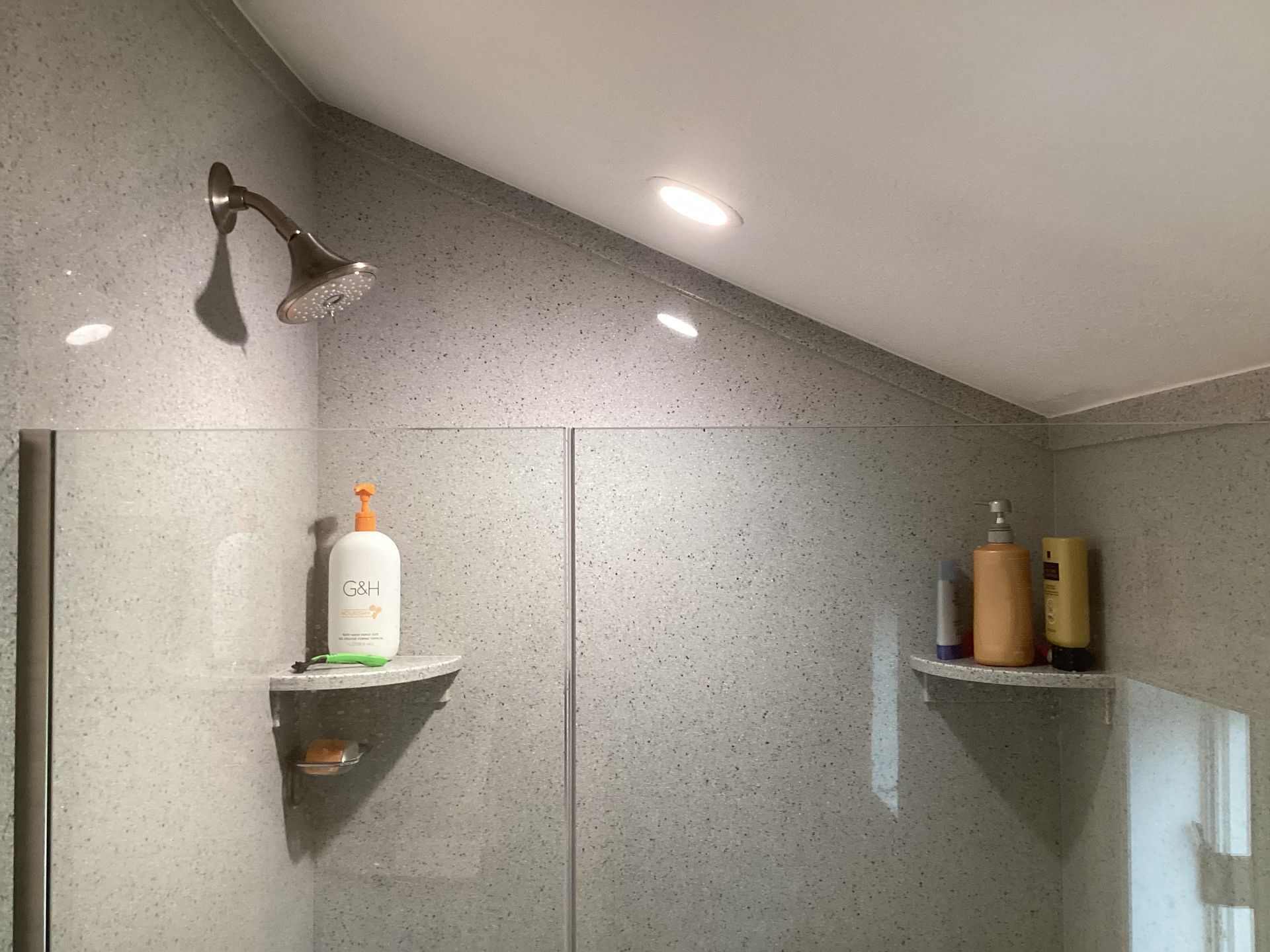 Shower stall with gray speckled walls, showerhead, and two shelves with bath products.