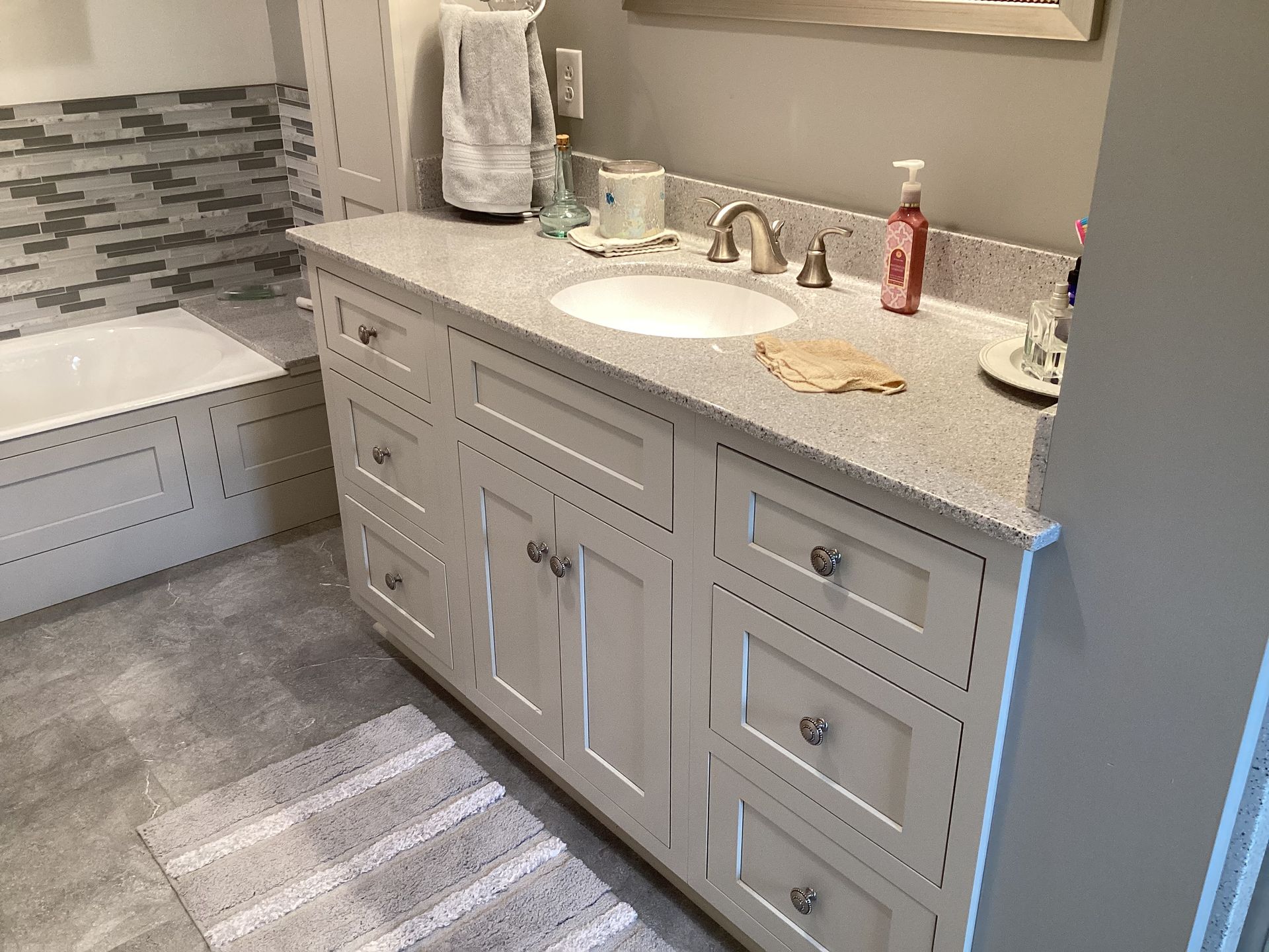 Bathroom with white cabinets, light countertop, round sink, and gray tile.