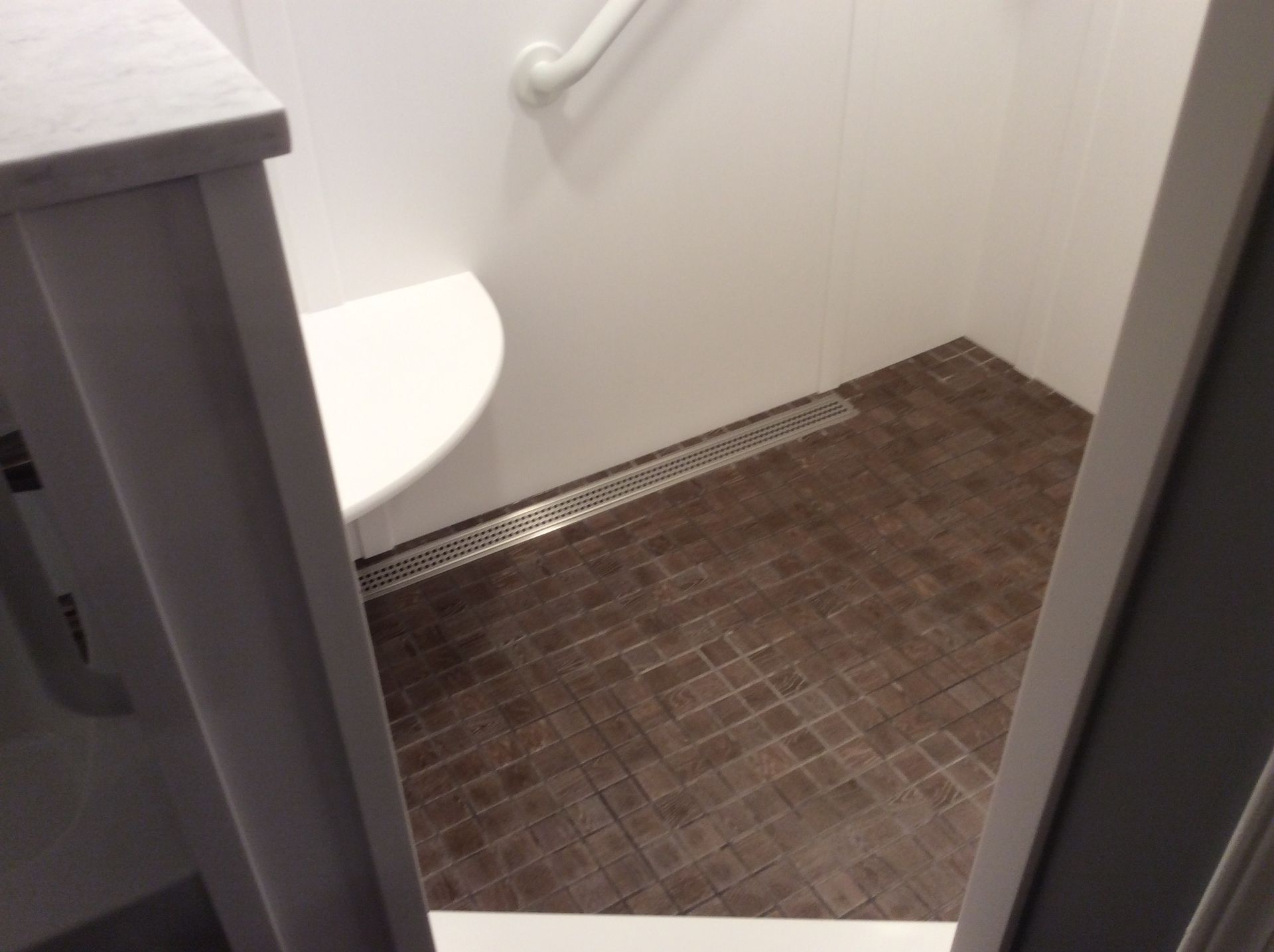 Accessible shower stall with brown tiled floor, white walls, and a grab bar.