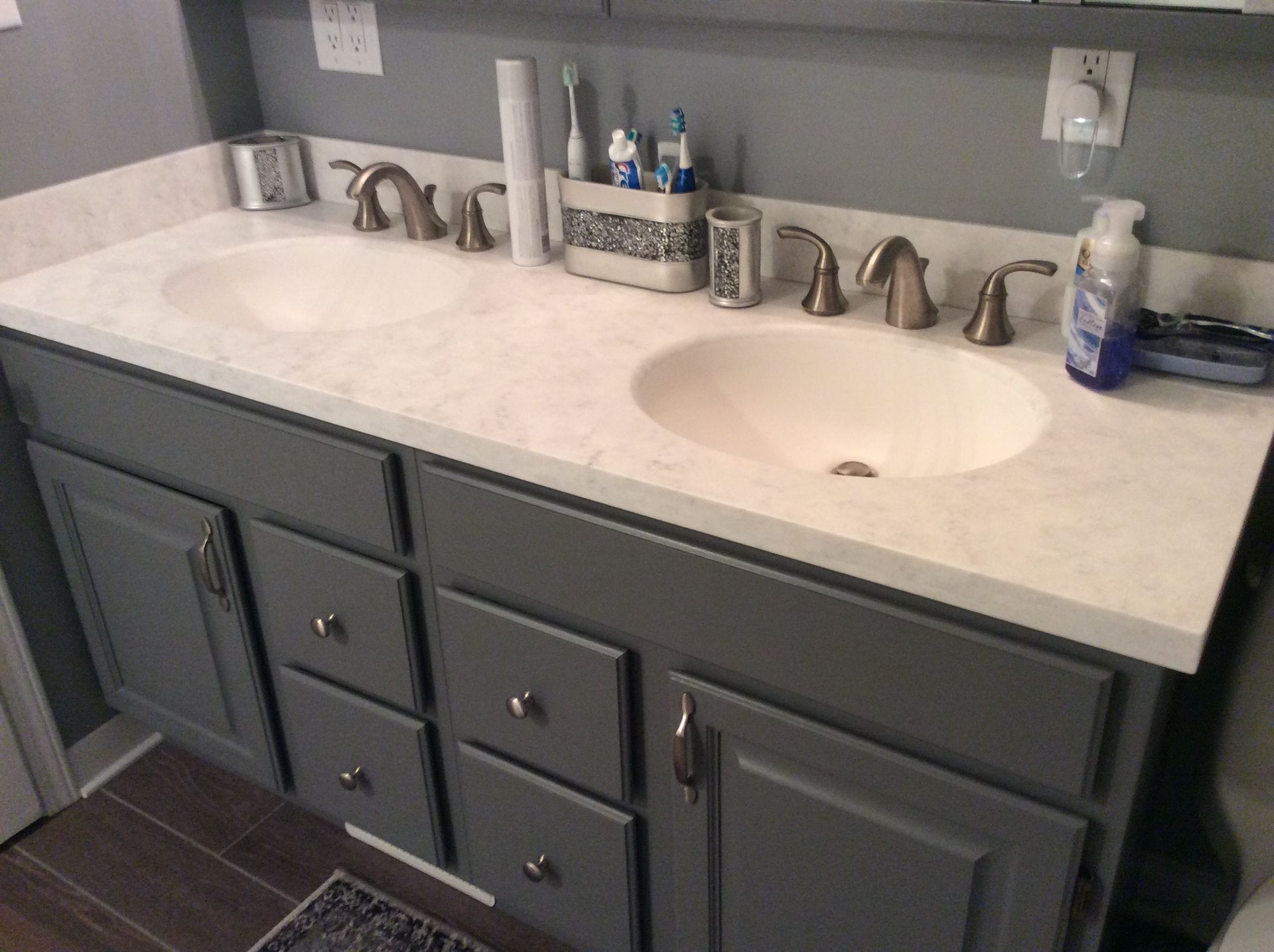 Gray double-sink bathroom vanity with white countertop, chrome fixtures, and accessories.