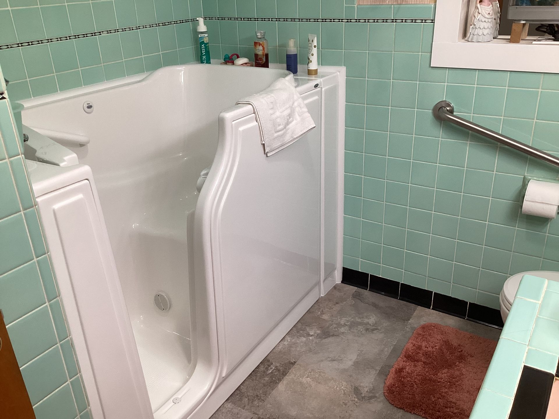 Walk-in bathtub in a bathroom with turquoise tile walls and a grab bar.