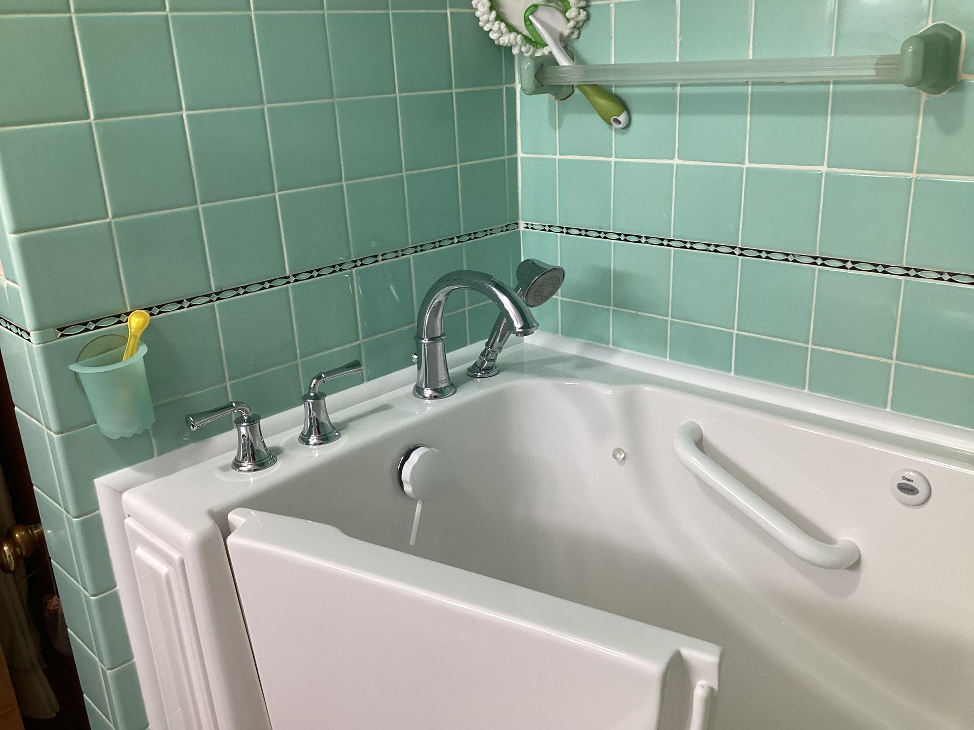 Walk-in bathtub with a seat and grab bar. Light green tile walls. Silver faucet and fixtures.