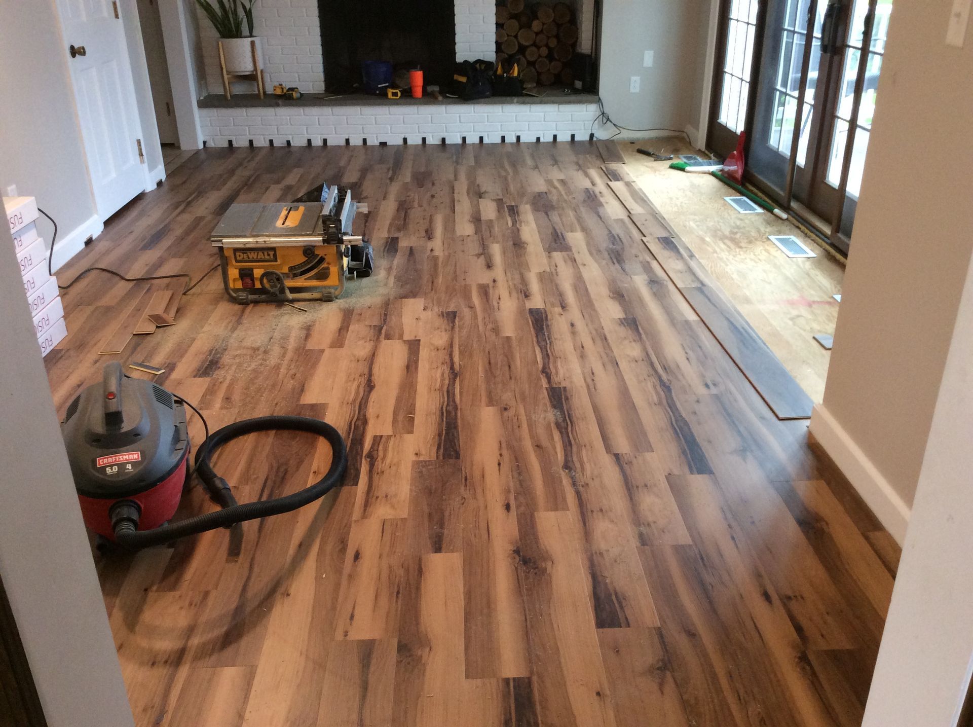 Installing laminate flooring; interior view of a room with saw, vacuum, and stacked flooring.