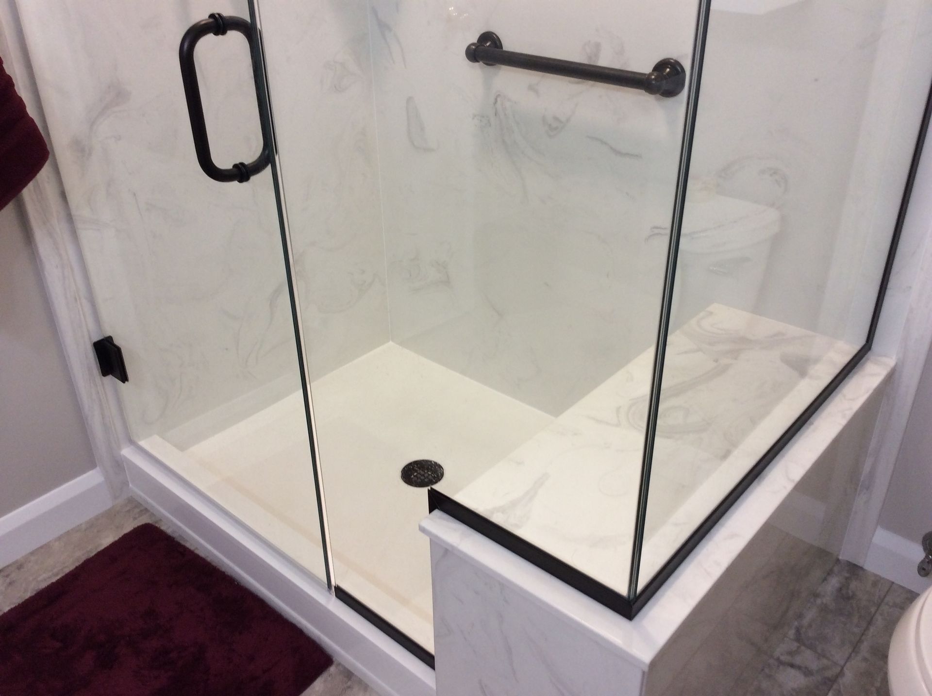 Shower with a marble-look bench and glass door, dark handle and grab bar.