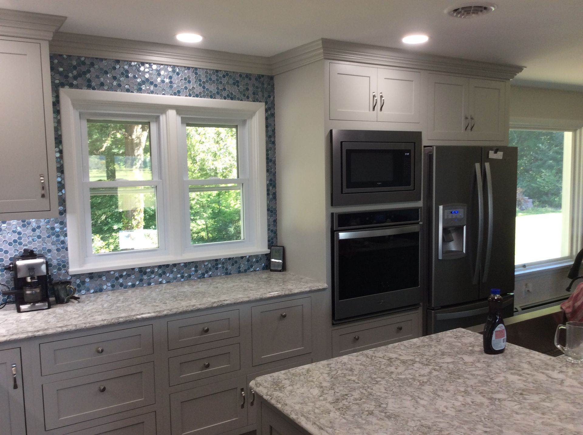 Kitchen with white cabinets, blue tile backsplash, stainless steel appliances, and a granite countertop island.