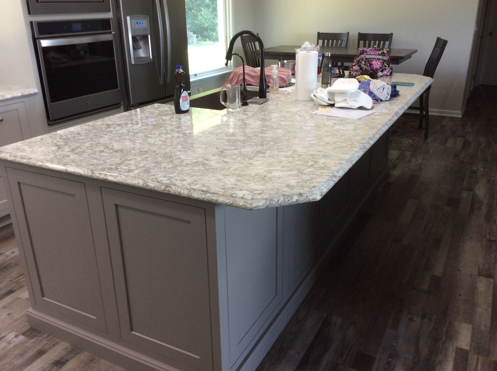 Kitchen island with light-colored countertop and grey cabinets; sink, faucet, and various items on top.