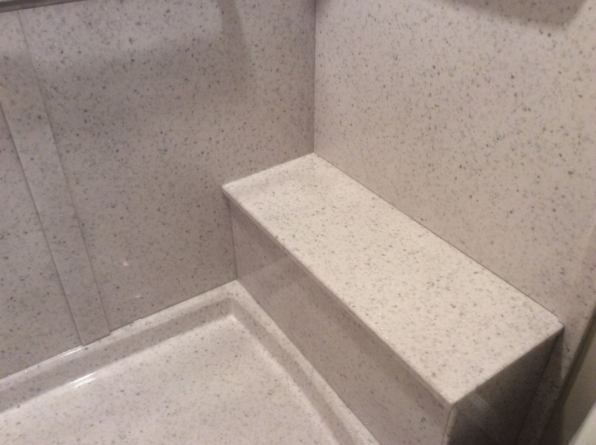Shower with a built-in bench, beige speckled surfaces.