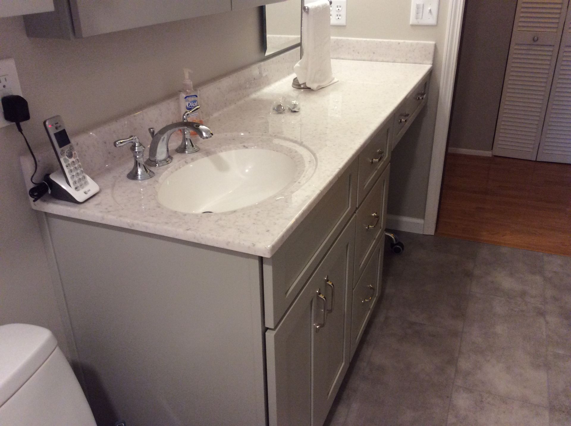Bathroom vanity with white countertop, sink, faucet, and cabinet storage. Toilet is in view.