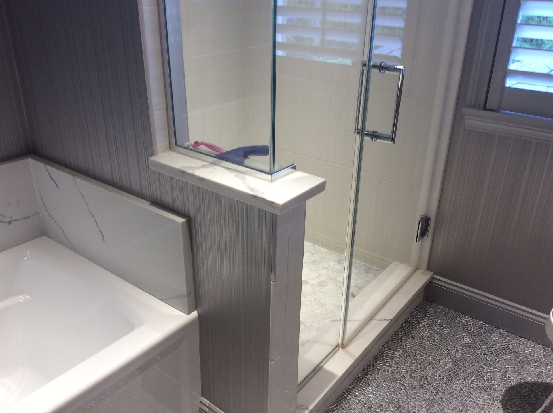 Modern bathroom with glass shower, white vanity, and marble accents. Silver-toned wallpaper and sparkly floor.