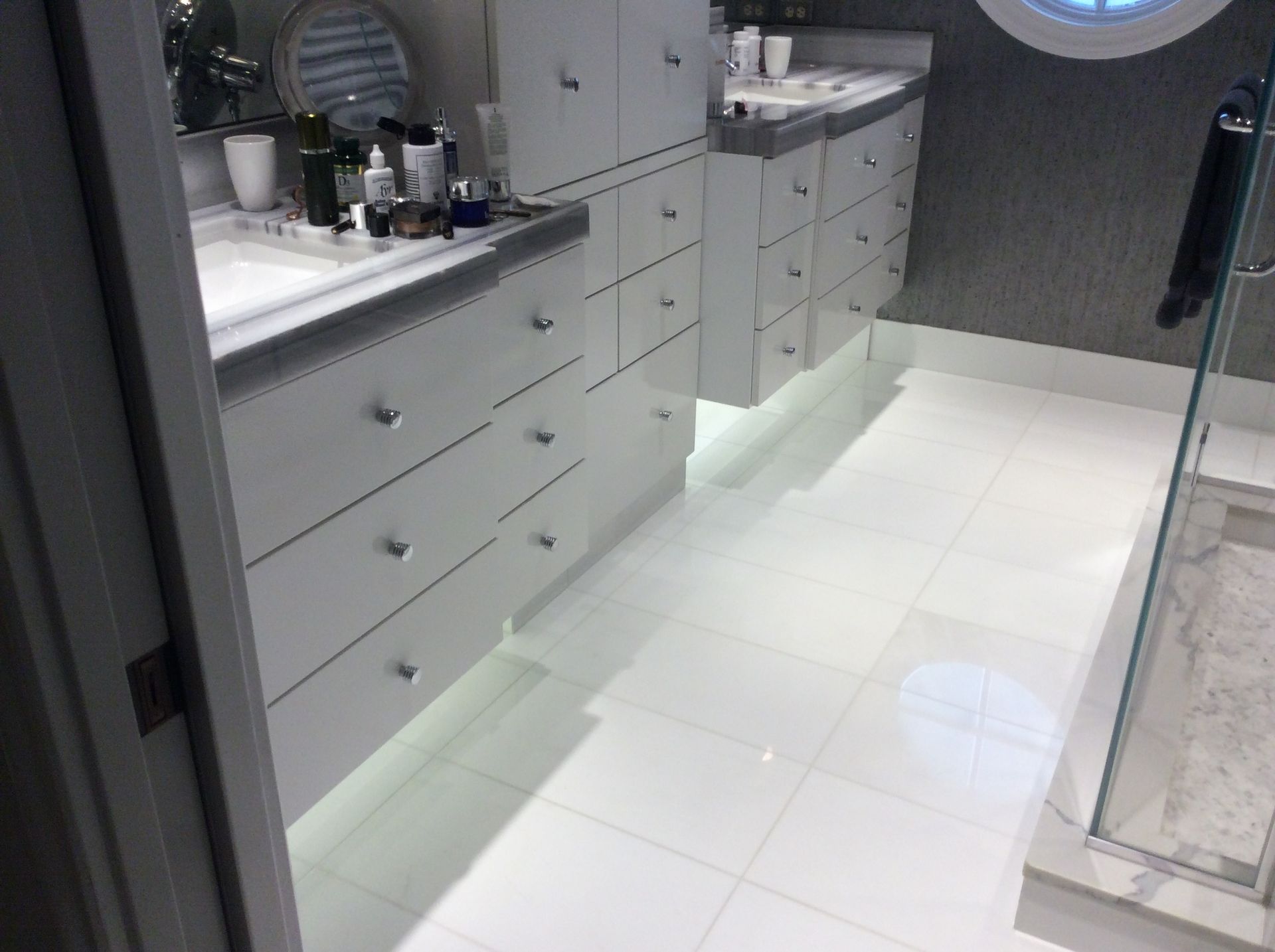 White bathroom with floating vanities, under-cabinet lighting, and glossy white floor tiles.