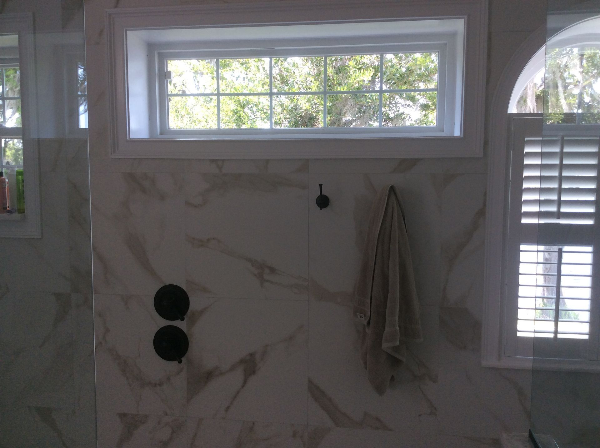 Bathroom with marble-patterned tile, a small window, black fixtures, and a towel hanging on the wall.