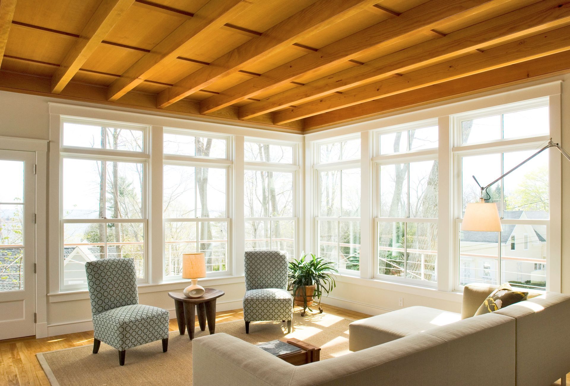 Living room with white-framed windows, wood ceiling, and cream-colored sofa. Two patterned chairs face a small table.