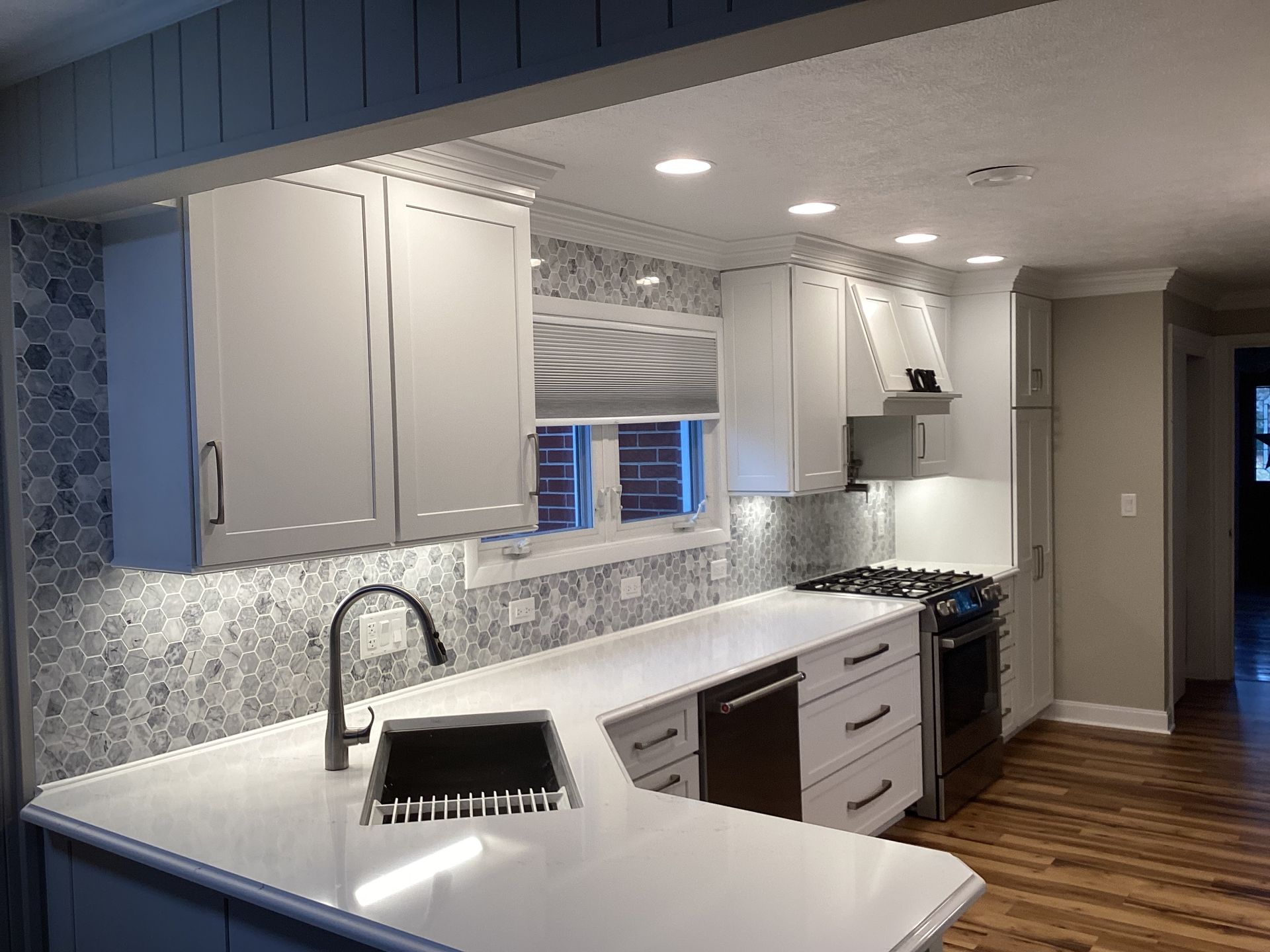 Modern kitchen with white cabinets, countertops, and gray backsplash.
