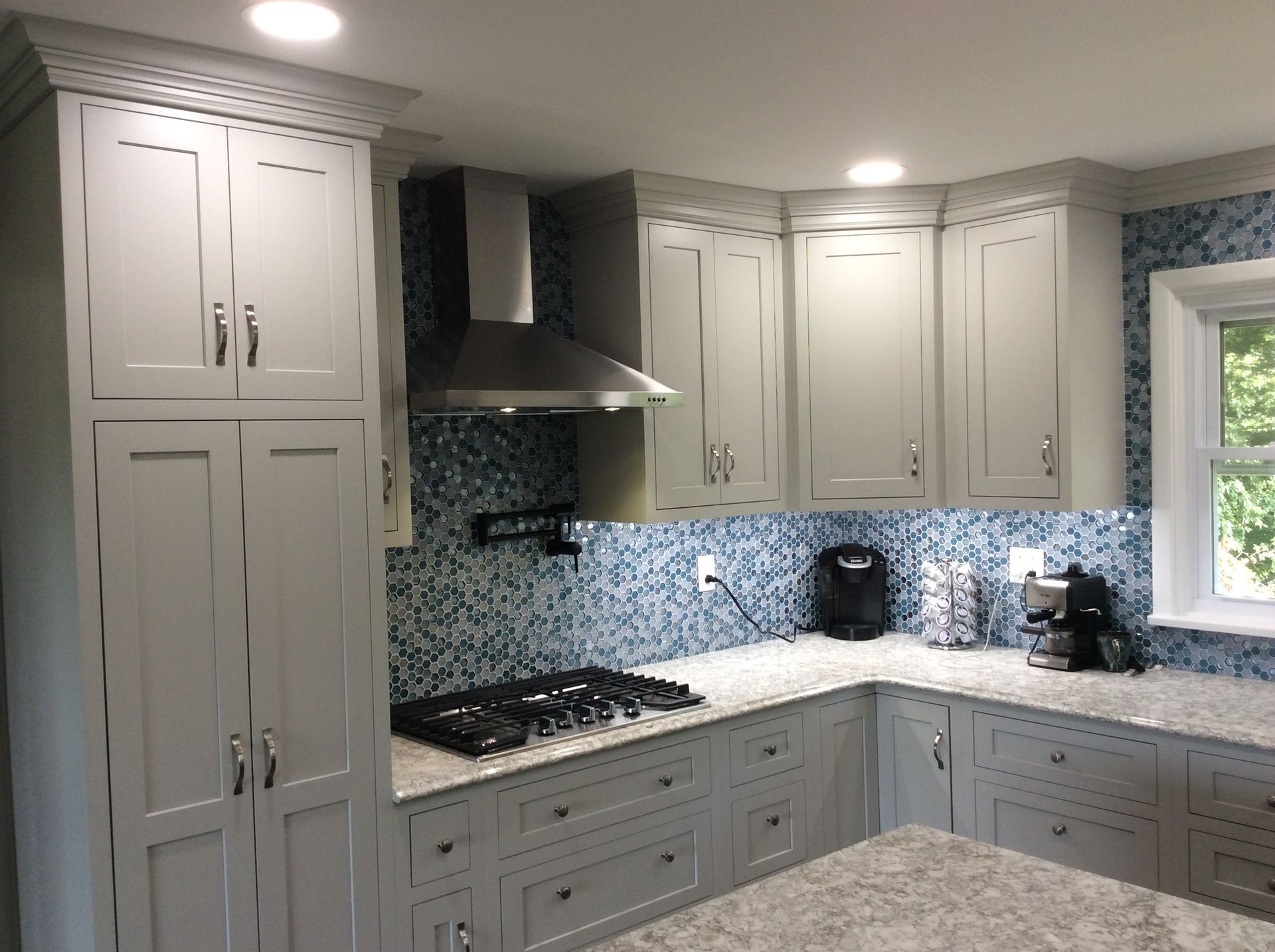 Gray kitchen cabinets with a stainless steel range hood and blue tile backsplash.