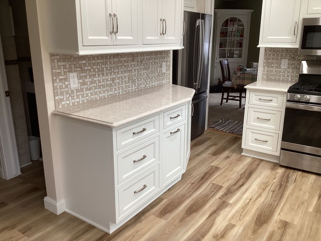 White kitchen cabinets, countertop, and mosaic tile backsplash with wooden floor.
