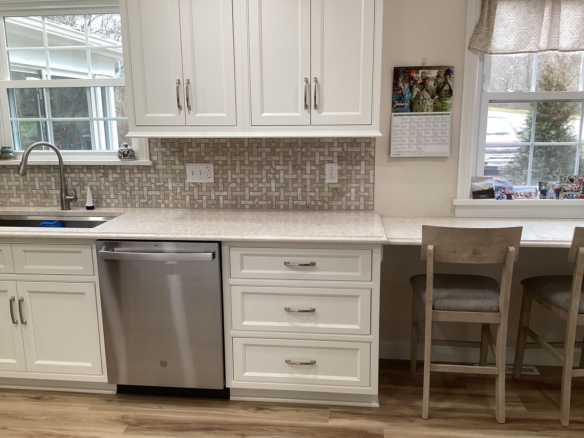 Kitchen with white cabinets, stainless steel appliances, neutral backsplash, and a small counter with bar stools.