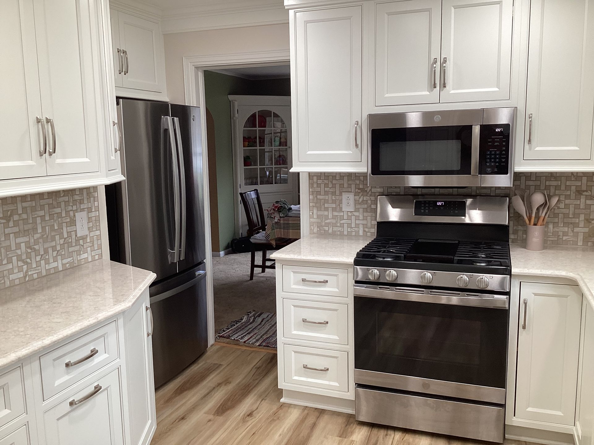 White kitchen with stainless steel appliances, light countertops, and wood-look flooring.