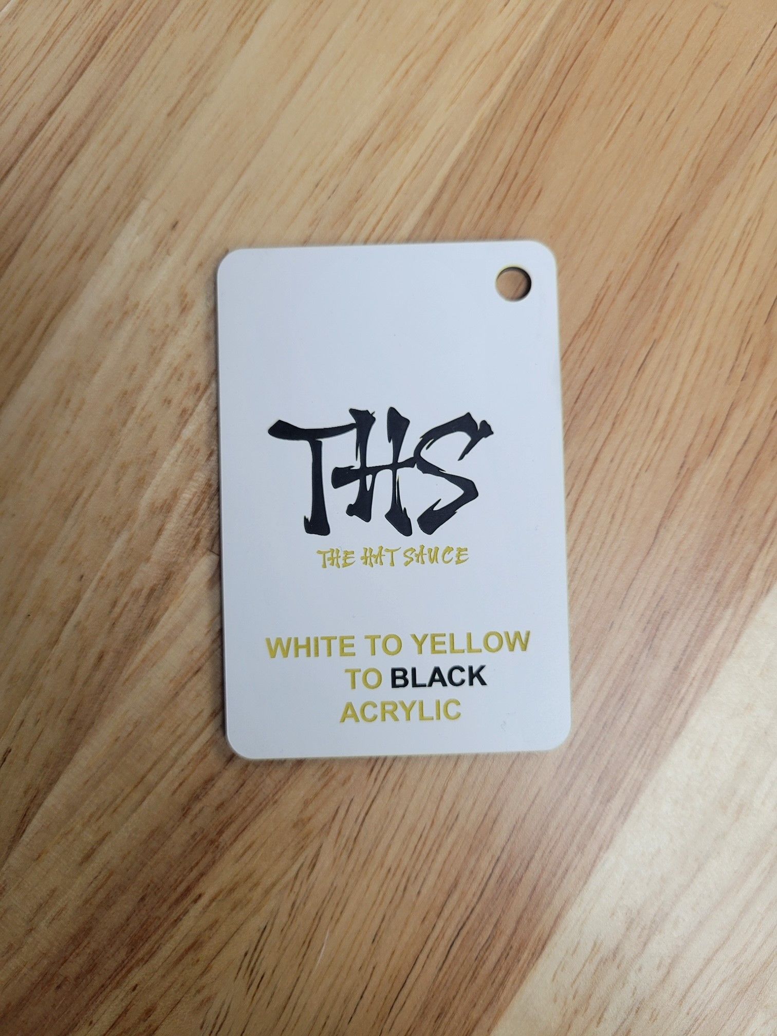 A white to yellow to black acrylic tag is sitting on a wooden table.