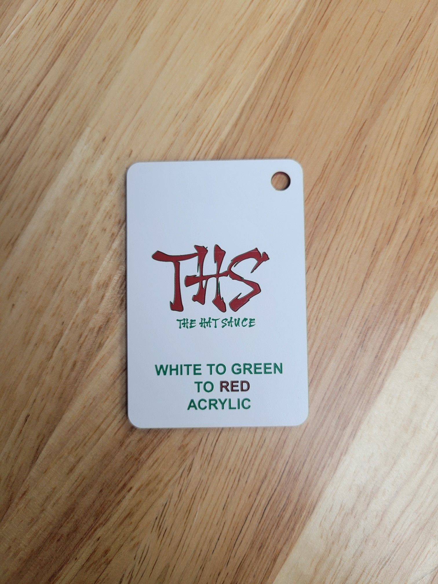 A white to green to red acrylic tag is sitting on a wooden table.