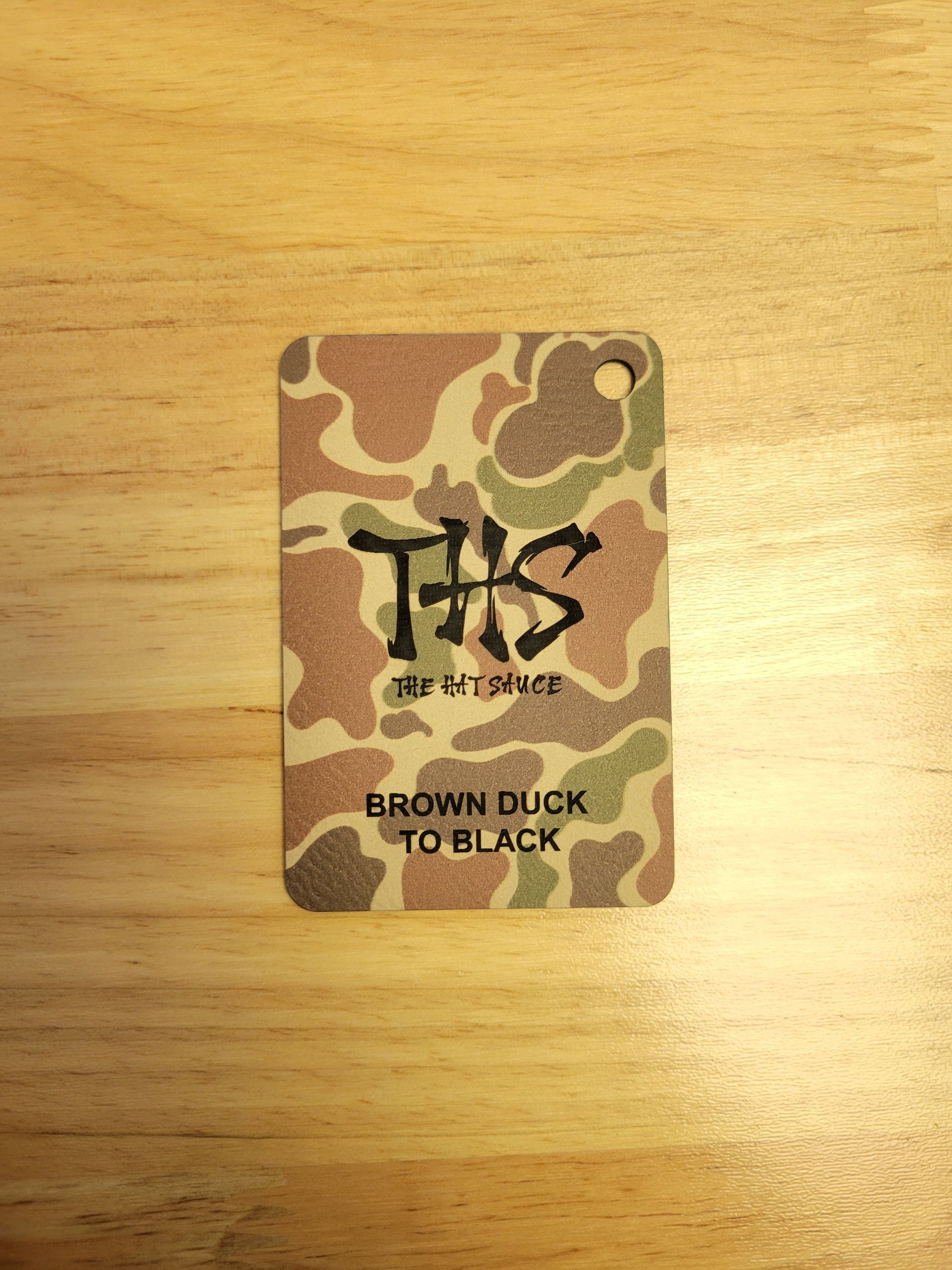 A brown duck to black tag is sitting on a wooden table.