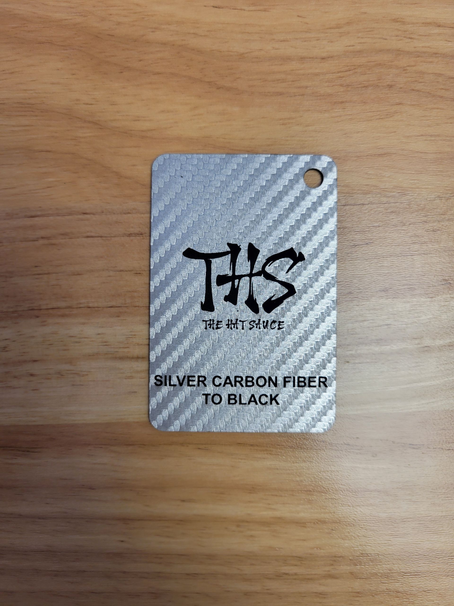 A silver carbon fiber tag is sitting on top of a wooden table.
